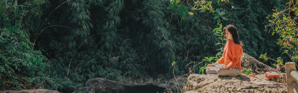 Woman meditating near a river in a forest.
