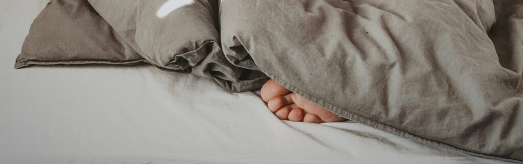 Toes poking out from gray comforter in bed