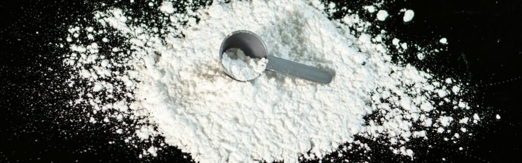 A pile of creatine on a smooth black counter with a grey plastic scoop on top.