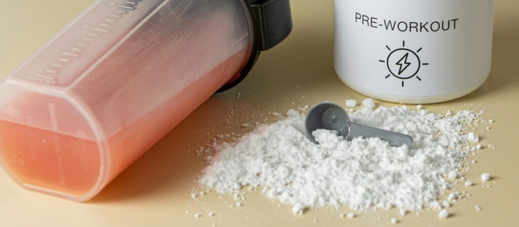 Pre-workout powder on a table next to a transparent shaker bottle with pink liquid inside