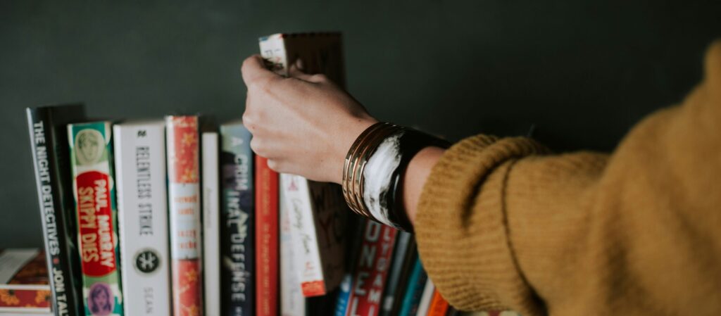 Woman in yellow sweater grabbing book off of a bookshelf