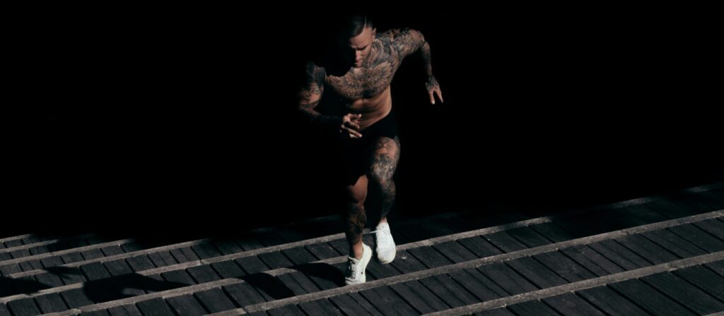 Tatted man running up stairs out from the darkness