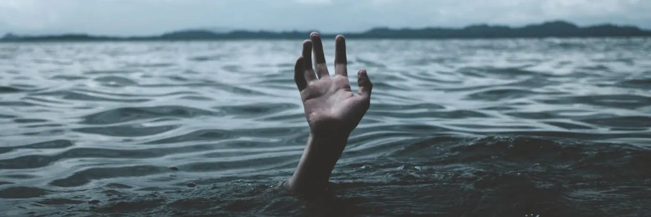 Hand emerging from dark blue water with dark clouds overhead