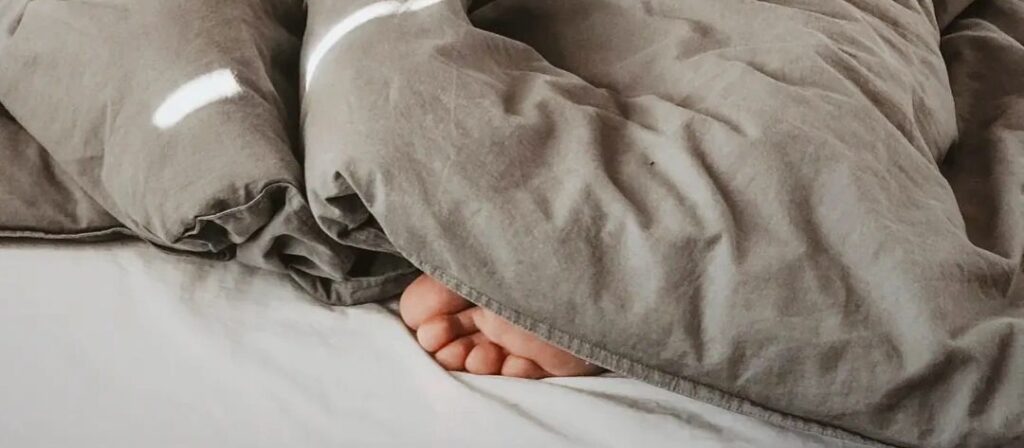 Toes sticking out from under a grey comforter