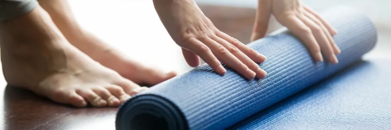 Woman bending down to roll up a blue yoga mat