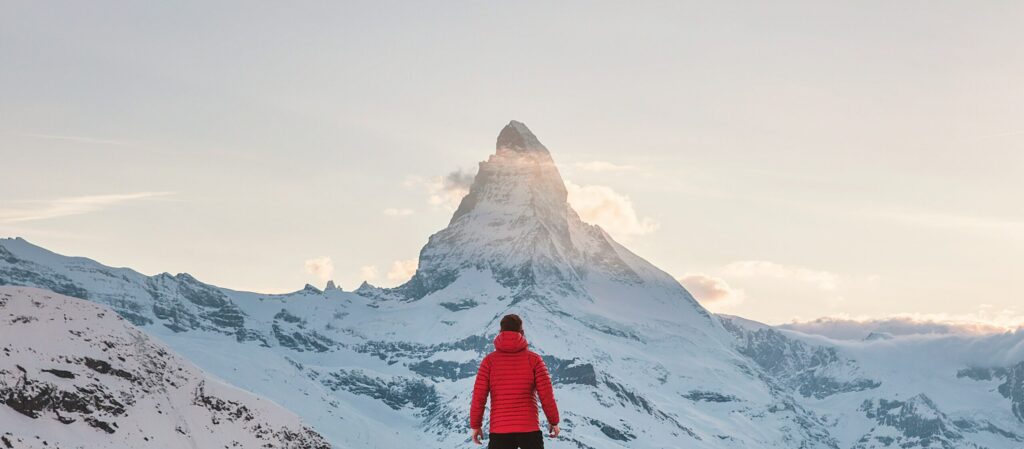 Man in red jacket standing at the foot of the mountain